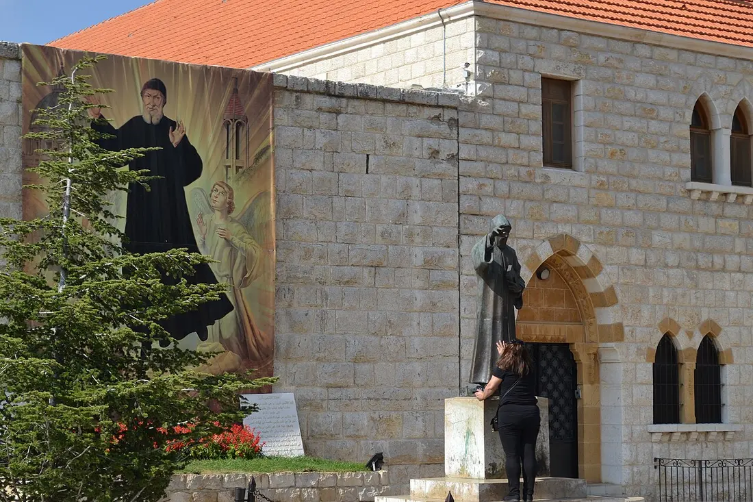 Pilger am Klostereingang von Annaya vor einer Statue des heiligen Charbel.