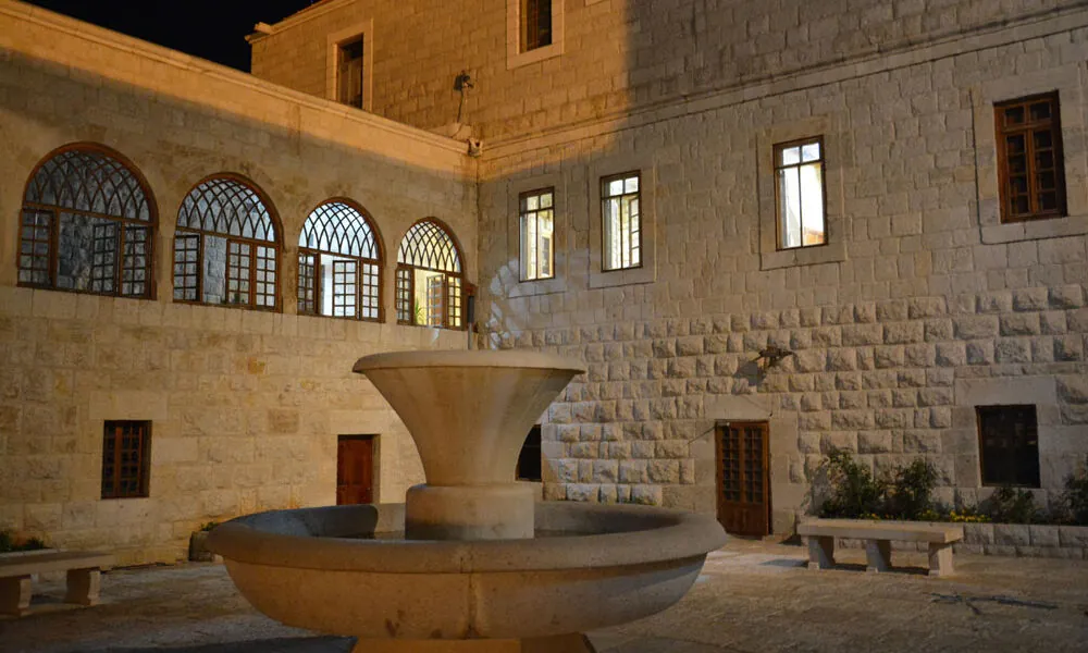 The stone monastery courtyard at Annaya at night, with arched windows and a round stone fountain